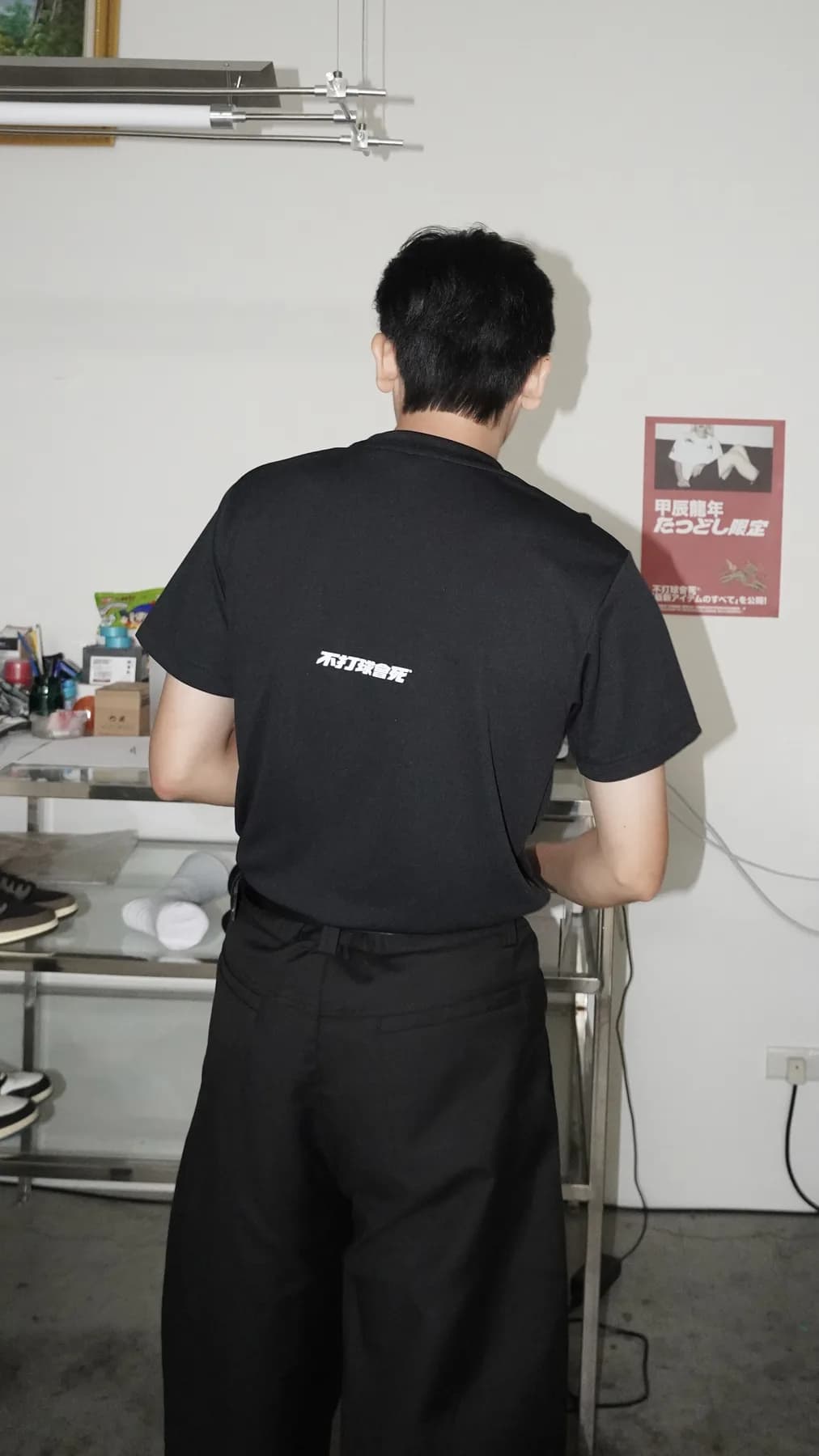 模特站立穿著黑色基礎素 T 的背面版型照